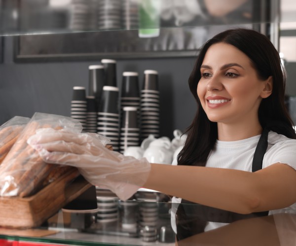 Smiling woman wearing gloves arranging packaged baked goods